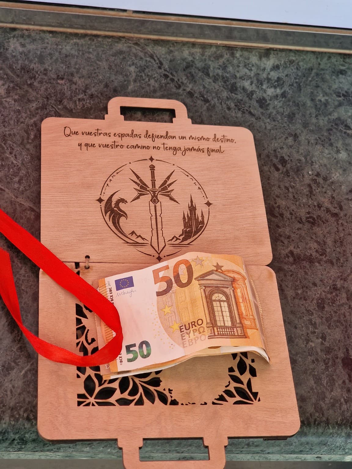 La misma maleta abierta con sus dos asas completas, uniones de cuerda, dedicatoria interior, lazo rojo y billetes