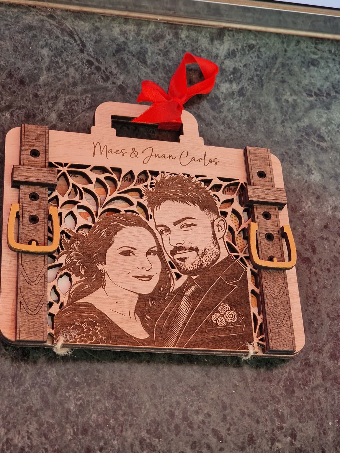 Maleta cerrada de Maes y Juan Carlos, con retrato grabado, calado vegetal, correas de madera y lazo rojo